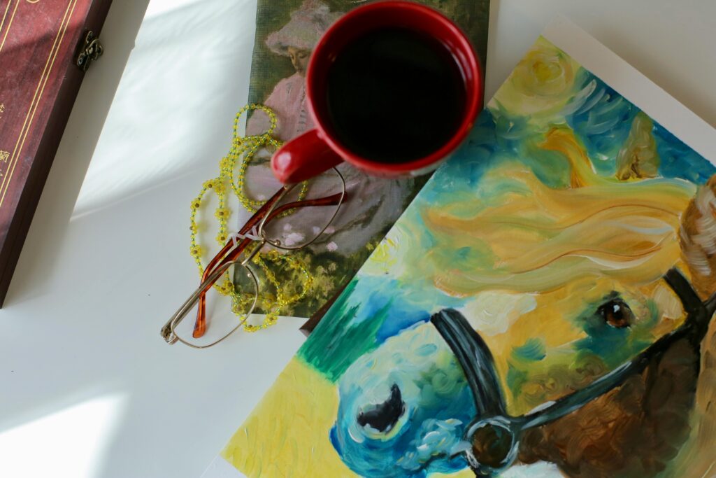 pexels photo 24960497 24960497 A vibrant still life featuring a coffee cup, colorful horse painting, and eyeglasses on a table.